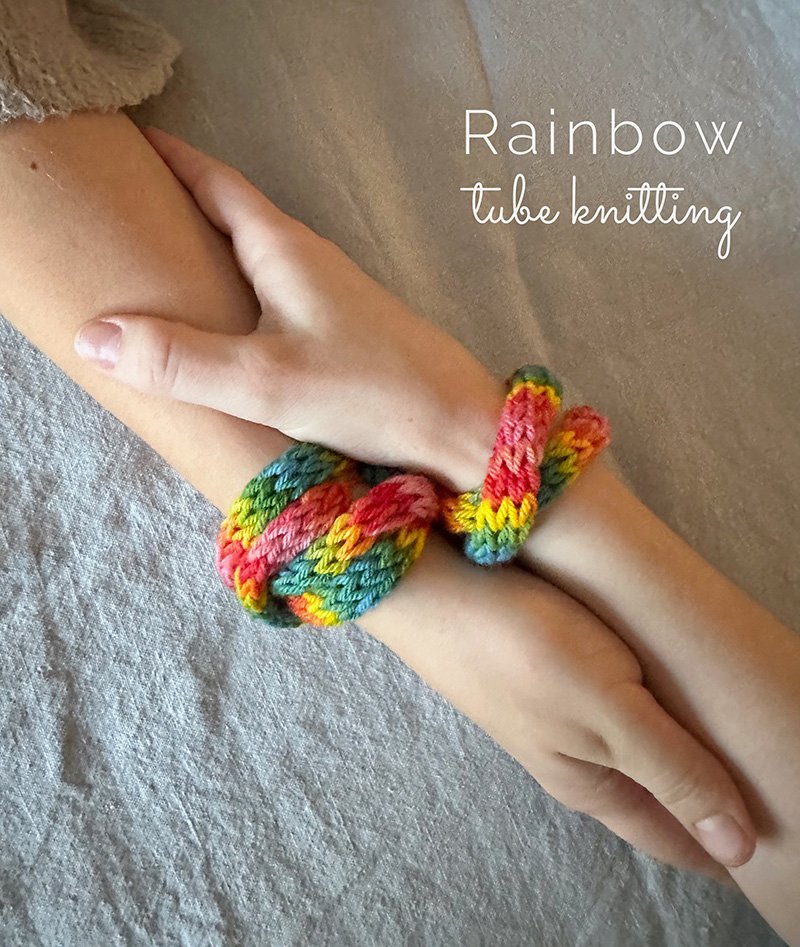 Rainbow tube knitted bracelents wrapped around two hands holding each other.